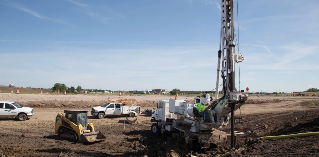 Action Electric foundation drilling crew with pressure digger rig, skid steer and service trucks on a Sioux Falls jobsite
